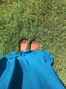 Brown skinned feet with red toenails on green grass.
